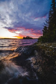 the sun is setting over some water and trees