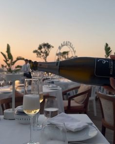 a bottle of wine being poured into a glass at an outdoor dining table with white linens