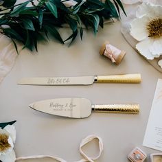 two gold colored kitchen knives on top of a table next to flowers and other items