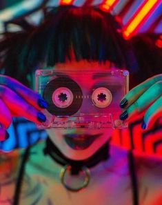 a woman holding up a cassette in front of her face with two eyeballs on it