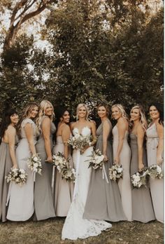 a group of women standing next to each other in front of trees and bushes with bouquets