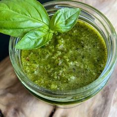 a glass jar filled with pesto sauce on top of a wooden table next to a green leaf