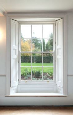 an open window in a white room with wood flooring and green grass behind it