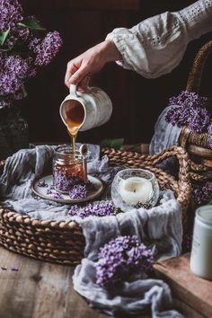 a person pouring tea into a cup on a table with purple flowers in the background