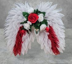 a red and white feather headpiece with roses on it's side, sitting on a stone surface