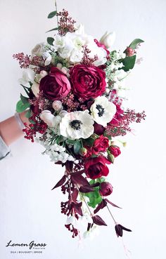 a bridal bouquet with red and white flowers is held by someone's hand