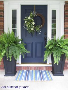 two planters are sitting on the front porch with a blue door and striped rug