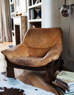 a brown leather chair sitting on top of a wooden floor next to a book shelf