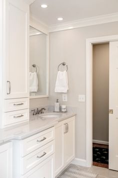 a bathroom with white cabinets and marble counter tops, along with an open door leading to another room