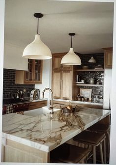 a kitchen with marble counter tops and two pendant lights hanging over the island in front of it