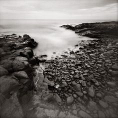 a black and white photo of rocks on the beach with water coming out of them