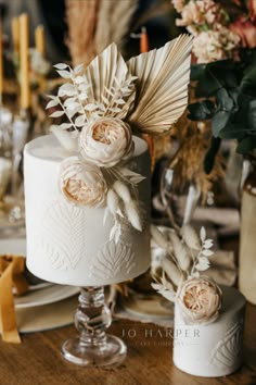 a wedding cake decorated with flowers and feathers on a table in front of some candles