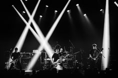 three people on stage playing instruments with lights coming from behind them and one person in the foreground