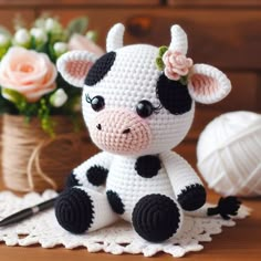 a crocheted cow sitting on top of a white doily next to flowers