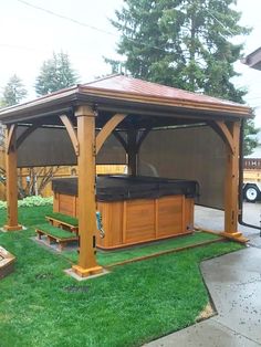 a wooden gazebo with a hot tub in the middle and grass on the ground