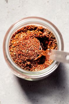 a jar filled with spices sitting on top of a white counter next to a spoon