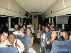 a group of people sitting in the back of a bus with their hands up and smiling