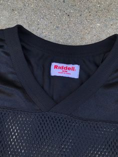 "Rock this amazing vintage black mesh jersey with a bold black leather pencil skirt. 100% Polyester Features modern aesthetic Brand: Riddell Estimate Size: M/L Listed Size: S/M Length: 24\" Bust: 46\" Waist: 46\"" Sporty Black T-shirt For Fall, Black Stretch 90s Tops, Black Stretch 90s Style Tops, 90s Style Black Stretch Tops, 90s Black Stretch T-shirt, 90s Style Stretch Black T-shirt, Black Stretch 90s Style T-shirt, Stretch Black T-shirt For Streetwear, Black Stretch T-shirt For Streetwear