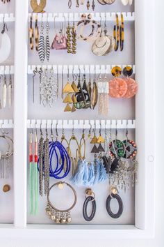 a white cabinet filled with lots of different types of earrings and bracelets on display