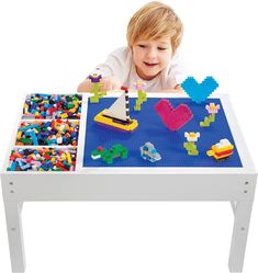 a young boy playing with legos on a white table and blue mat underneath him