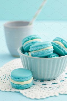 blue and white macaroons in a bowl on a doily next to a cup