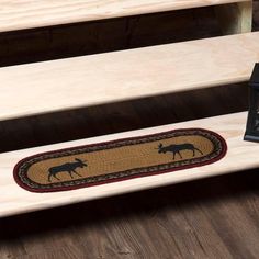 a clock sitting on top of two wooden steps next to a rug with moose silhouettes