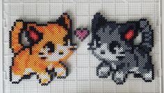 two cross stitch cats sitting next to each other on top of a white tile wall