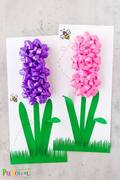 two paper flowers on top of a piece of paper with grass and bees in the background