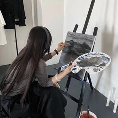 a woman is sitting in front of an easel and painting with headphones on