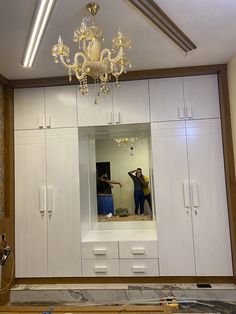 two people are taking pictures in the mirror while they work on an unfinished room with white cabinets