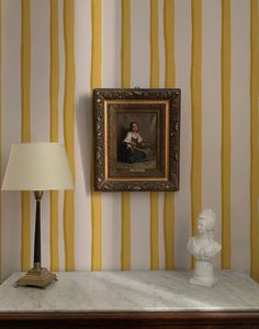 a painting is hanging on the wall next to a table with a lamp and busturine