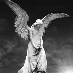 an angel statue with its wings spread out in front of a dark sky and clouds