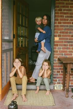 three children sitting on the front steps of a house with their hands in their mouths