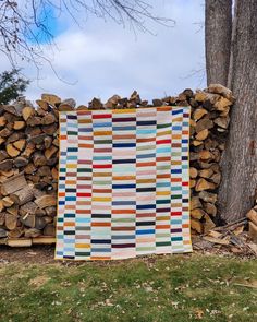 a quilt is hanging on a pile of firewood in front of a large tree