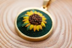 This dainty sunflower necklace is truly one of a kind. Handmade in the UK, each one is slightly different making it entirely unique to you. Stitched using the finest threads and Japanese beads on 100% cotton fabric, the design is mounted into a gold plated frame with matching 18" inch, 18K gold plated chain.  The pendant measures roughly 2cm in diameter. The necklace can be made to order on any fabric colour. To keep the necklace looking great for years to come, please treat with care and avoid Gold Jewelry With Floral Embroidery For Gift, Handmade Yellow Gold Flower Necklaces, Hand Embroidered Necklace, Japanese Beads, Embroidered Necklace, Sunflower Necklace, Fabric Colour, Embroidery Floral, Floral Jewellery