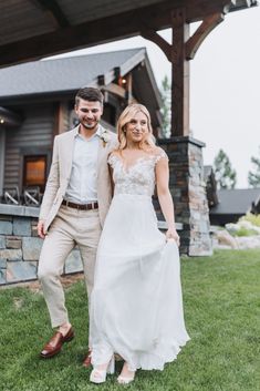 a bride and groom walking through the grass in front of a cabin at their wedding