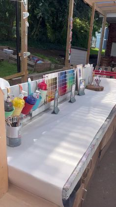 a long table covered with lots of paint and supplies on it's sides, in front of a house