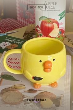 a yellow cup sitting on top of a table next to a carton of apple juice