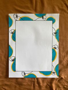 a piece of white paper with blue and yellow designs on it sitting on a bed