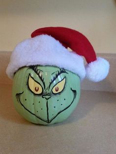 a green pumpkin with a red santa hat on it's head and eyes painted on