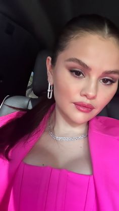 a woman with long hair wearing a pink top and silver earrings sitting in the back seat of a car