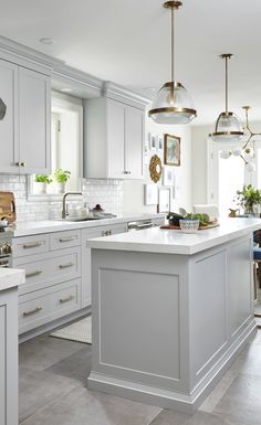 a kitchen with white cabinets and an island in the middle is decorated with hanging lights