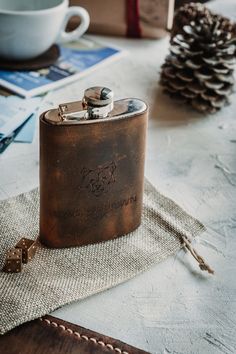 a leather flask is sitting on a table next to some pine cones and other items