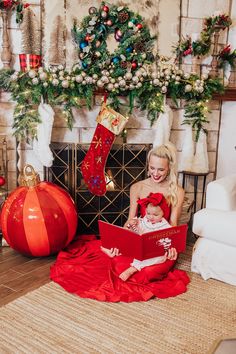 a woman and her baby are sitting in front of the fireplace with christmas decorations around them