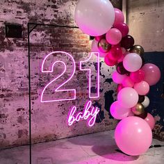 a pink and white balloon arch with the number twenty one baby on it in front of a brick wall