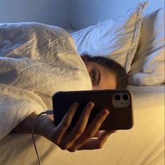 a woman is laying in bed and looking at her phone with an alarm clock on it