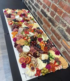 a large platter of fruit and cheese on a table next to a brick wall