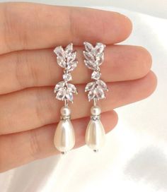 a pair of white pearl and crystal earrings on someone's hand with their fingers in the air