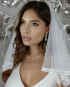 a woman wearing a white wedding veil and diamond earrings is looking at the camera while holding her hand out