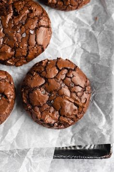 three chocolate cookies are sitting on wax paper with a knife next to it and one cookie has been cut in half